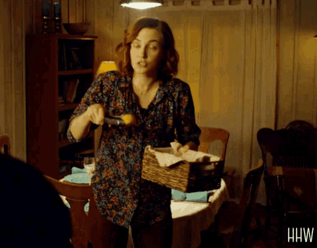 a woman in a floral shirt is holding a basket in front of a table with hhw written on the bottom right