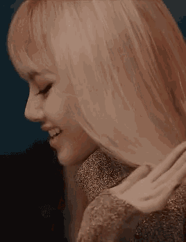 a close up of a woman with long blonde hair wearing a gold sweater and smiling .