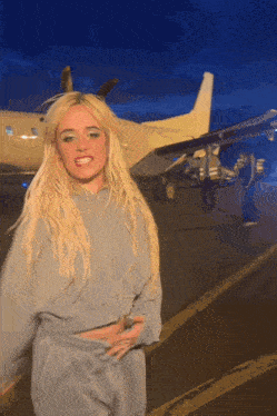a blonde woman is standing in front of a plane that says ' airways ' on the side