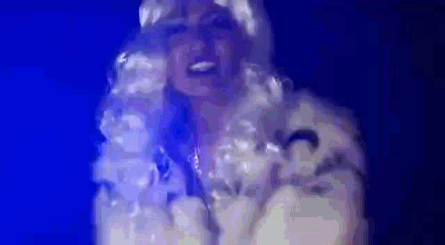 a woman in a white wig is standing in front of a blue background and smiling .