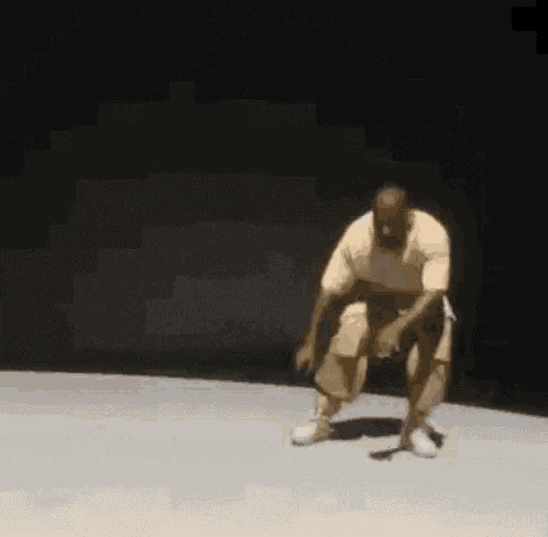 a man is kneeling down on a stage in a dark room and dancing .