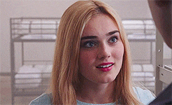 a woman with blonde hair and red lipstick is talking to a man in a room with bunk beds .