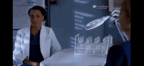 a woman in a lab coat is sitting at a table talking to another woman