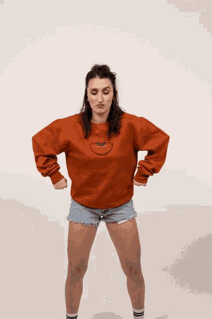 a woman wearing an orange sweater with a tomato embroidered on it
