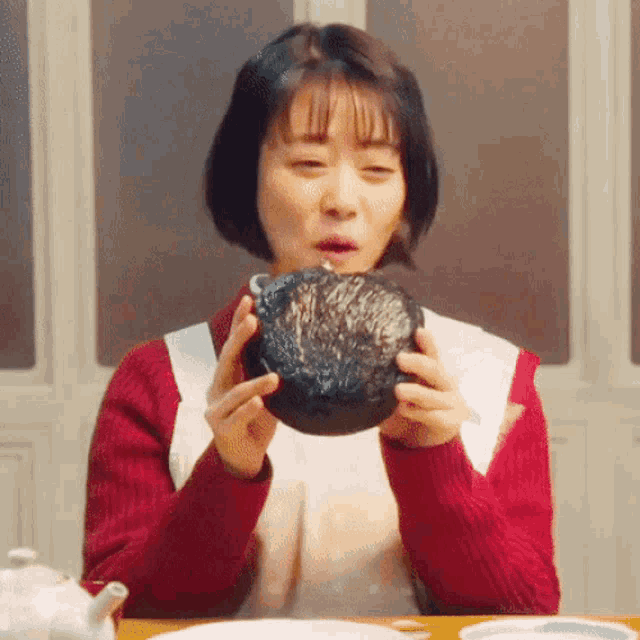 a woman is sitting at a table holding a bowl of food