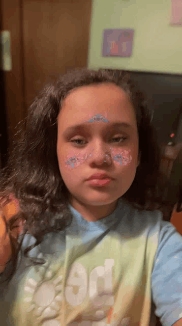 a girl with flowers painted on her face is wearing a shirt that says good