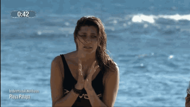 a woman in a black swimsuit stands in front of the ocean with the time of 1:42