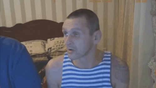 a man in a blue and white striped tank top is sitting in front of a bed