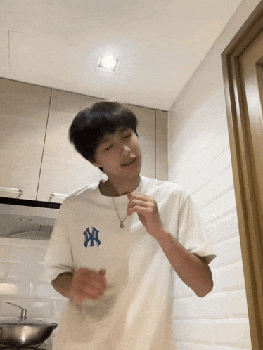 a young man wearing a white ny t-shirt is dancing in a kitchen