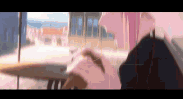 a woman with pink hair is sitting at a table in front of a window with a blurred background .