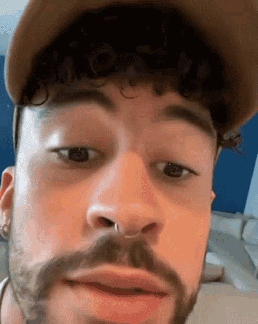 a close up of a man with a beard wearing a hat and earrings .