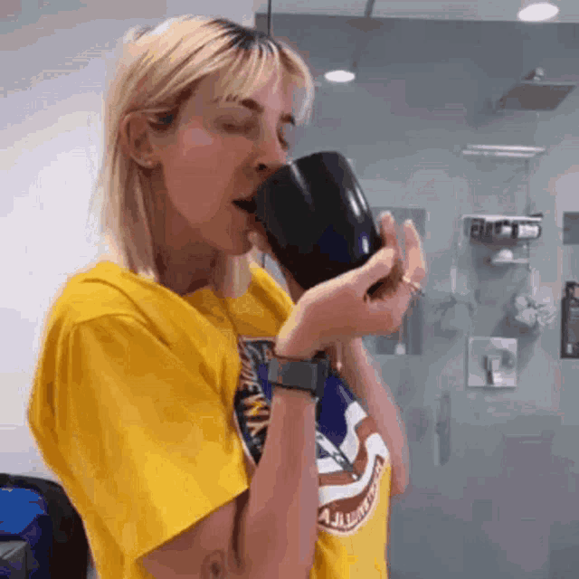 a woman in a yellow shirt is drinking from a cup