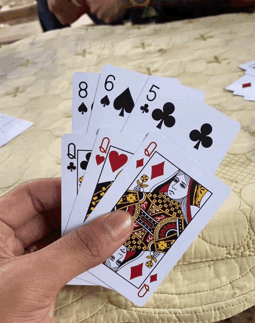 a hand holding four playing cards including the queen of hearts