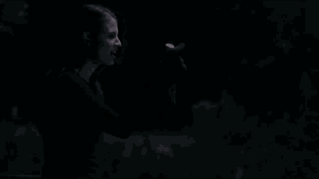 a woman in a black dress is standing in the dark looking at something .
