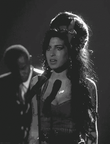 a woman singing into a microphone with a man playing a guitar in the background