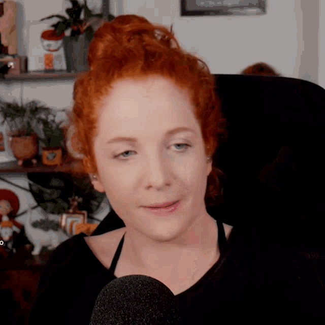 a woman with red hair sits in front of a black microphone
