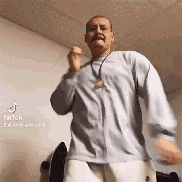 a man wearing a grey shirt and white shorts is dancing in a room with a skateboard in the background .