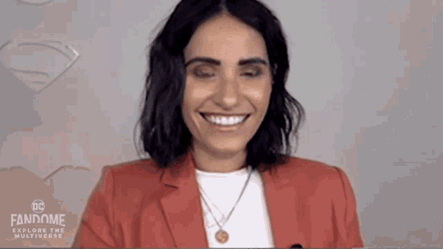 a woman wearing a red jacket and a white shirt is smiling with her eyes closed .