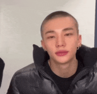 a young man with a shaved head is wearing a black jacket .