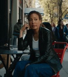 a woman in a leather jacket sits at a table with a cigarette in her hand