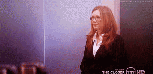 a woman wearing glasses and a suit is standing in front of a sign that says the closer tnt hd