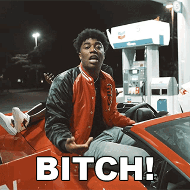 a man in a red and black jacket is sitting in a red car with the words bitch written on it