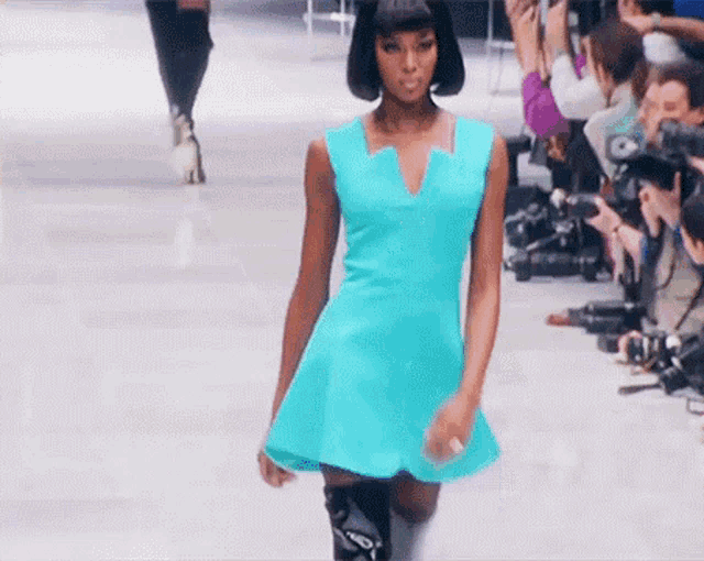 a model in a blue dress is walking down the runway at a fashion show .