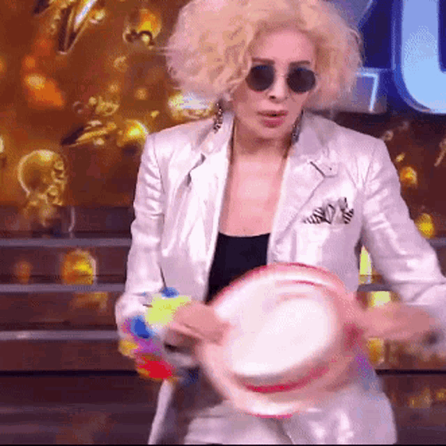 a woman wearing sunglasses and a white jacket holds a tambourine