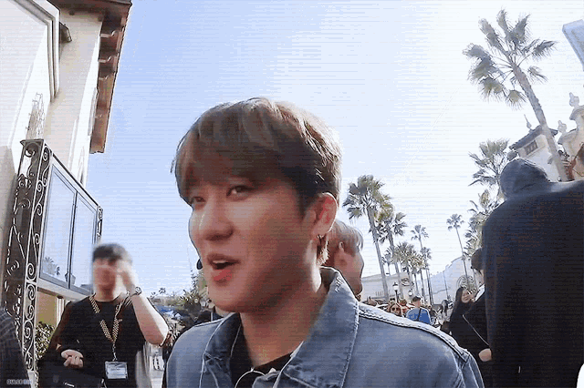 a young man wearing a denim jacket is walking down a street with palm trees in the background .