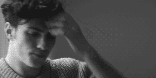 a black and white photo of a man wearing a sweater holding his hair .