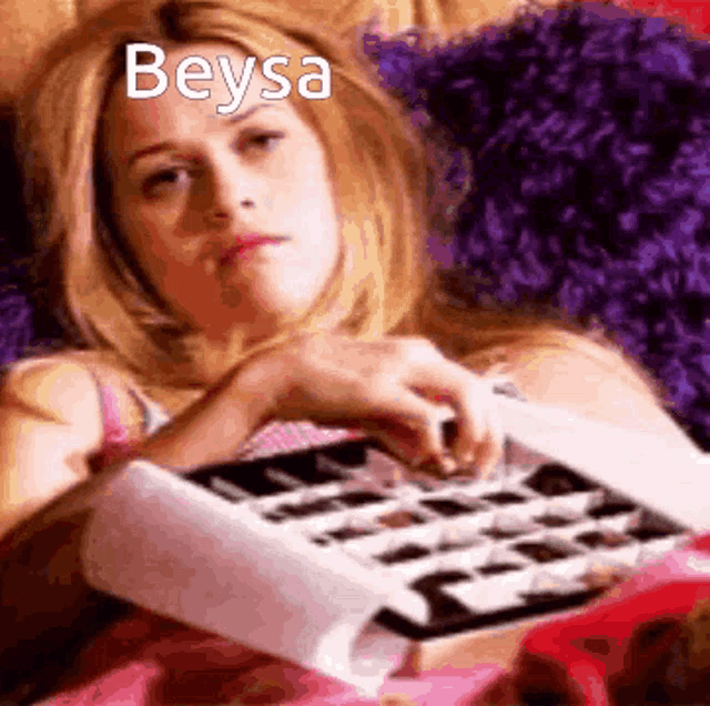 a woman is laying on a bed holding a box of chocolates and the name beysa is on the bottom