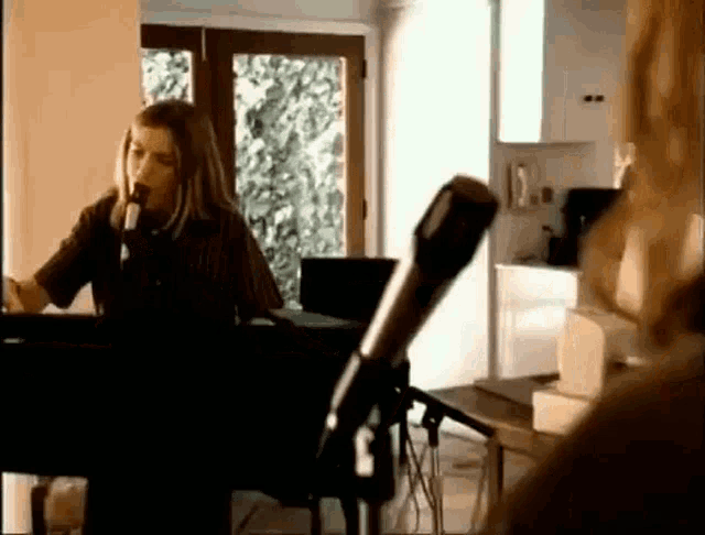 a woman is singing into a microphone while playing a piano in a room .