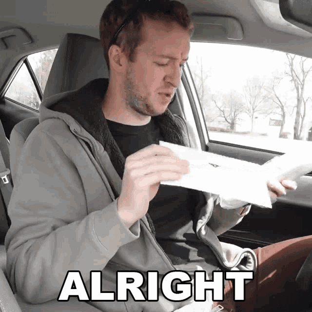 a man in a car is holding a piece of paper and the word alright is on the bottom