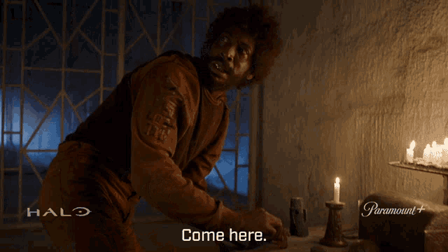 a man is standing in a room with candles and a halo logo behind him