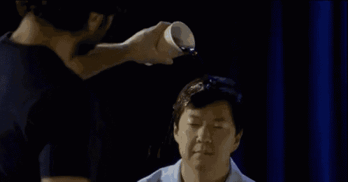 a man is pouring a cup of liquid on another man 's head .