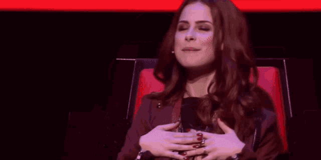 a woman is sitting in a red chair with her hands on her chest .