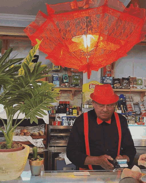 a man wearing a red hat and suspenders is behind a counter with a bag of lays chips behind him