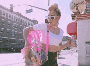 a woman is walking down the street with a pink bag and a can of soda