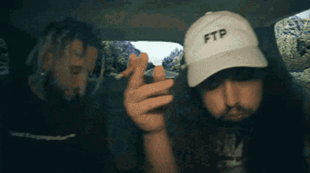 two men in a car one wearing a white hat that says ftp