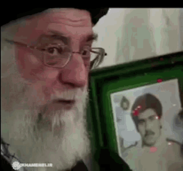 a man with glasses and a beard is holding a framed picture of a man with a mustache .