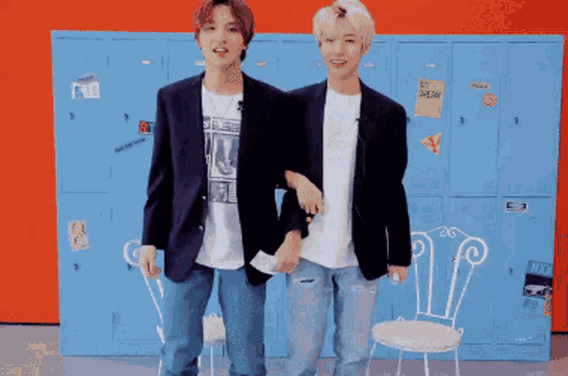 two young men are standing next to each other in front of blue lockers and chairs .