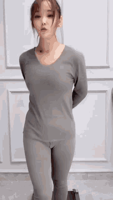 a woman in a grey shirt and leggings is standing in front of a wall .