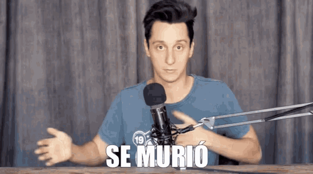 a man in a blue shirt stands in front of a microphone with the words se murio written above him