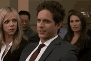 a man in a suit and tie is sitting in front of a group of women .