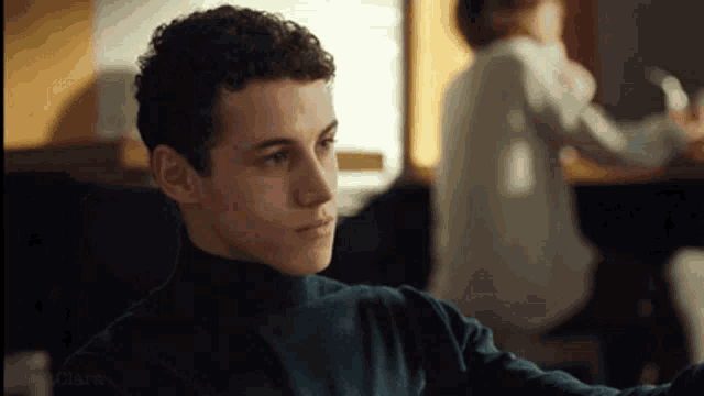 a young man with curly hair wearing a blue turtleneck