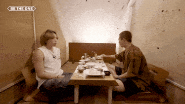 two men sit at a table with a sign that says be the one on it
