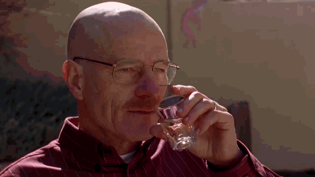 a bald man with glasses and a mustache drinks from a glass