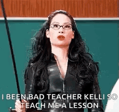 a woman in a black suit and glasses is holding a cane in front of a green board .