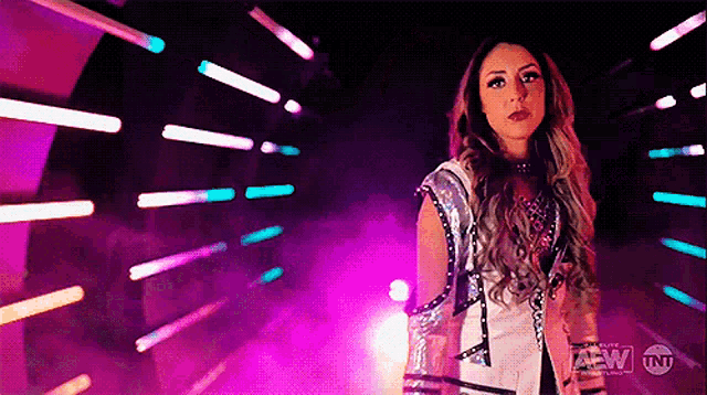 a woman in a wrestling outfit is standing in a dark room with purple lights behind her .