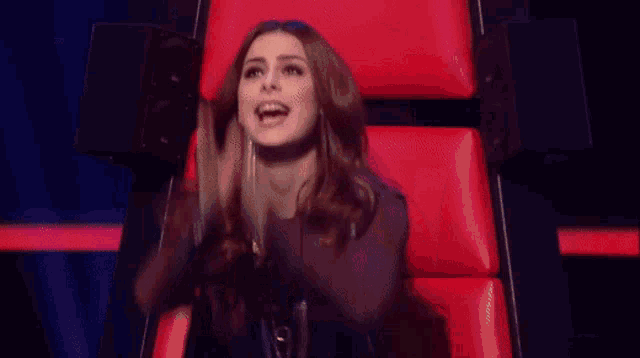 a woman is sitting in a red chair with her hands in her mouth .